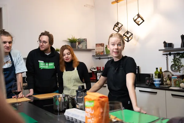 Elīna stāsta pieaugušo grupai pie virtuves galda